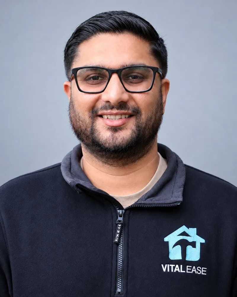 A smiling Vital Ease team member with glasses and a beard, in a black branded quarter-zip