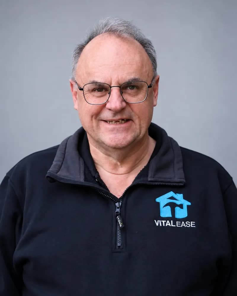 A Vital Ease team member with glasses and grey hair, in a black branded quarter-zip