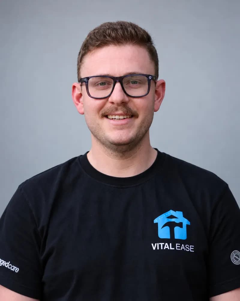 A Vital Ease team member with glasses and a moustache, in a black branded T-shirt