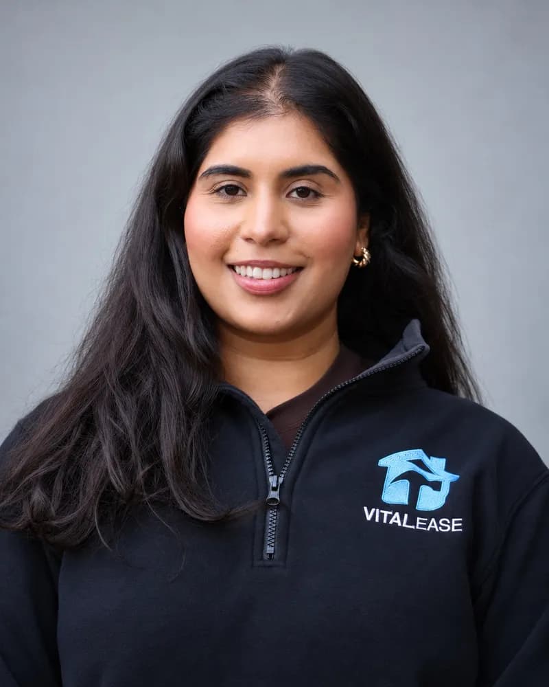 A smiling Vital Ease team member with long dark hair and gold earrings, in a black branded quarter-zip