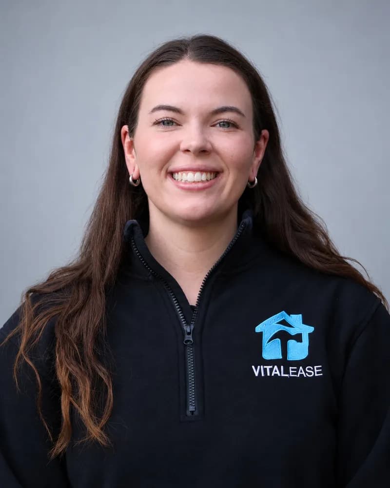A smiling Vital Ease team member with long dark hair, in a black branded quarter-zip