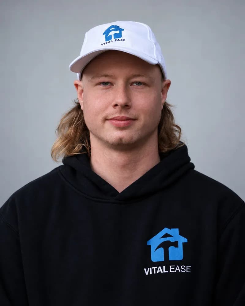 A Vital Ease team member with long fair hair, in a white branded cap and black hoodie