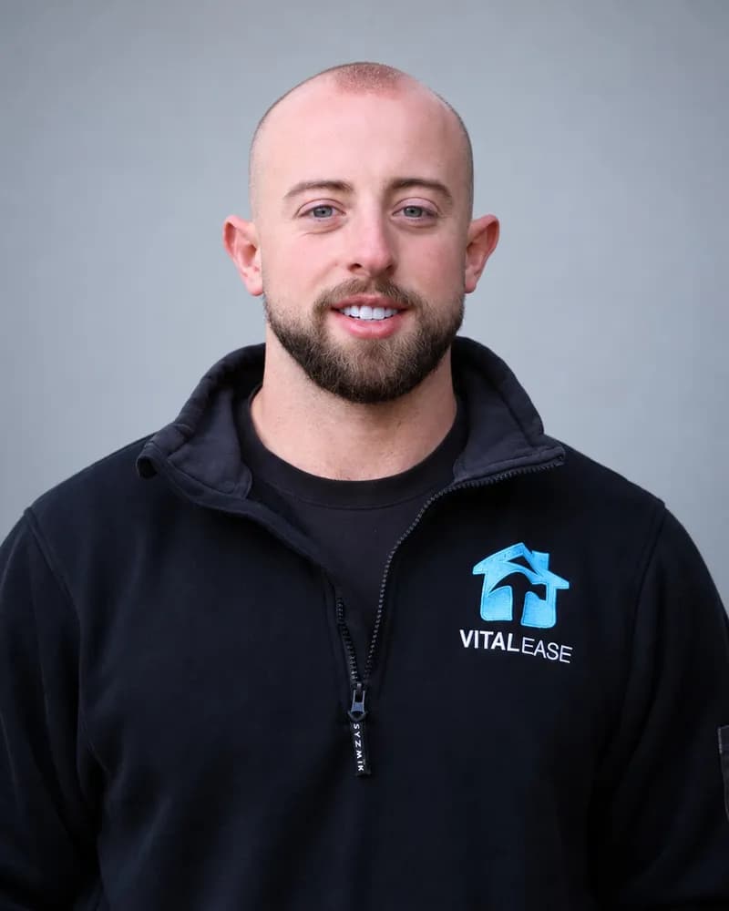 A Vital Ease team member with a shaved head and short beard, in a black branded quarter-zip