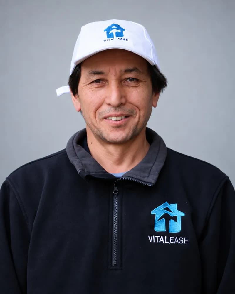 A smiling Vital Ease team member in a white branded cap and black quarter-zip